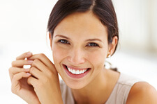 Brunette woman smiling with hands together next to face