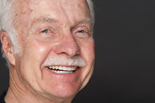 Older man with grey hair and mustache smiling