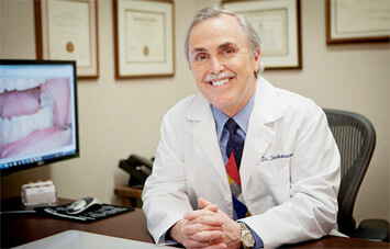 Dr. Charles Briscoe smilig at desk in white coat